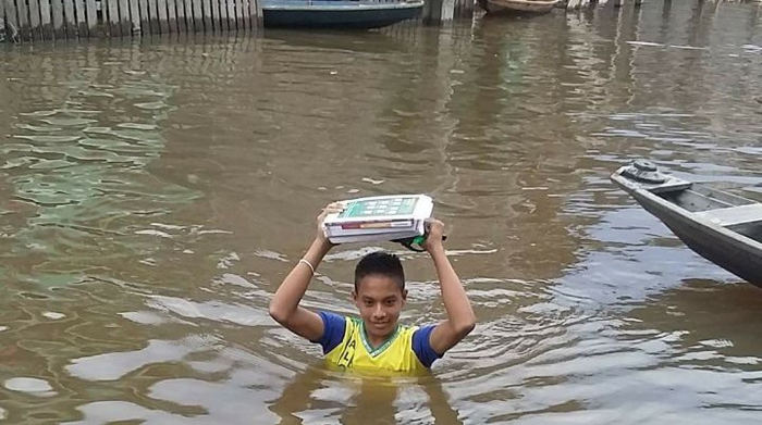 Estudantes carregam livros na cabeça na ida à escola durante cheia no Amazonas